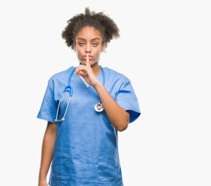 Young afro american doctor woman over isolated background asking to be quiet with finger on lips. Silence and secret concept.